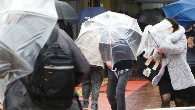 雨と風をしのぎながら歩く人達